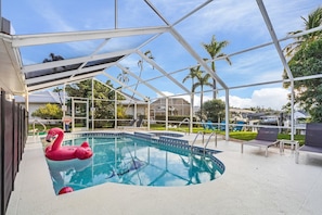 A swimming pool with a pink flamingo float, surrounded by lounge chairs and a covered area with a metal frame.