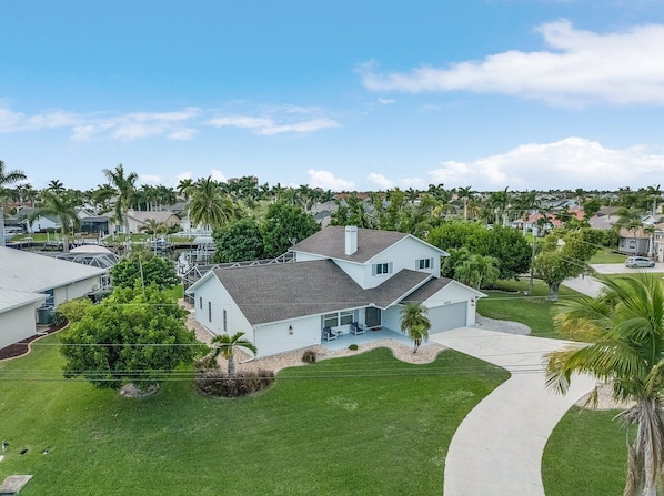 A two-story house with a covered patio, surrounded by a well-maintained lawn and palm trees.