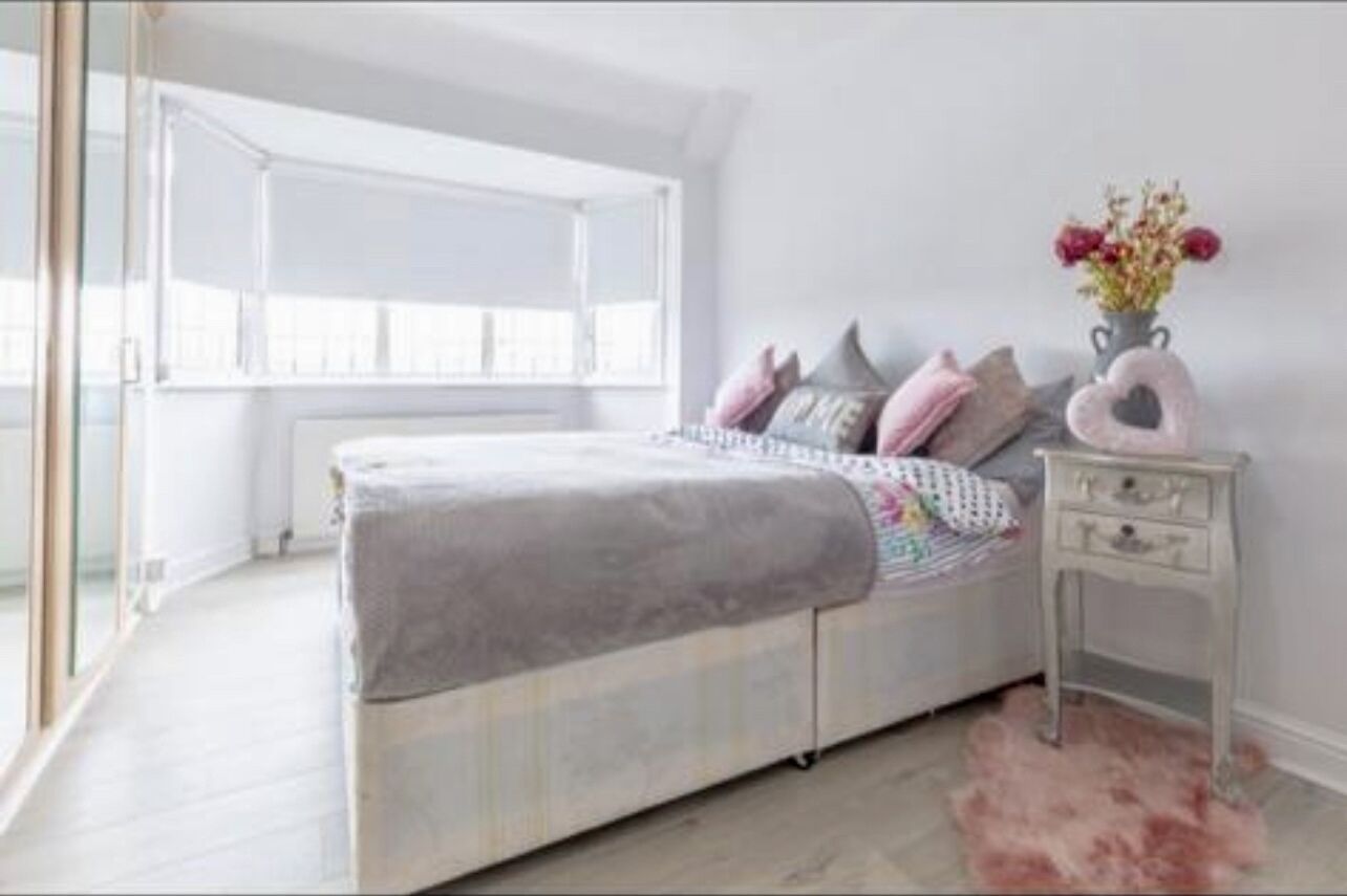 A bedroom with a bed, a nightstand, a window, and a pink rug.