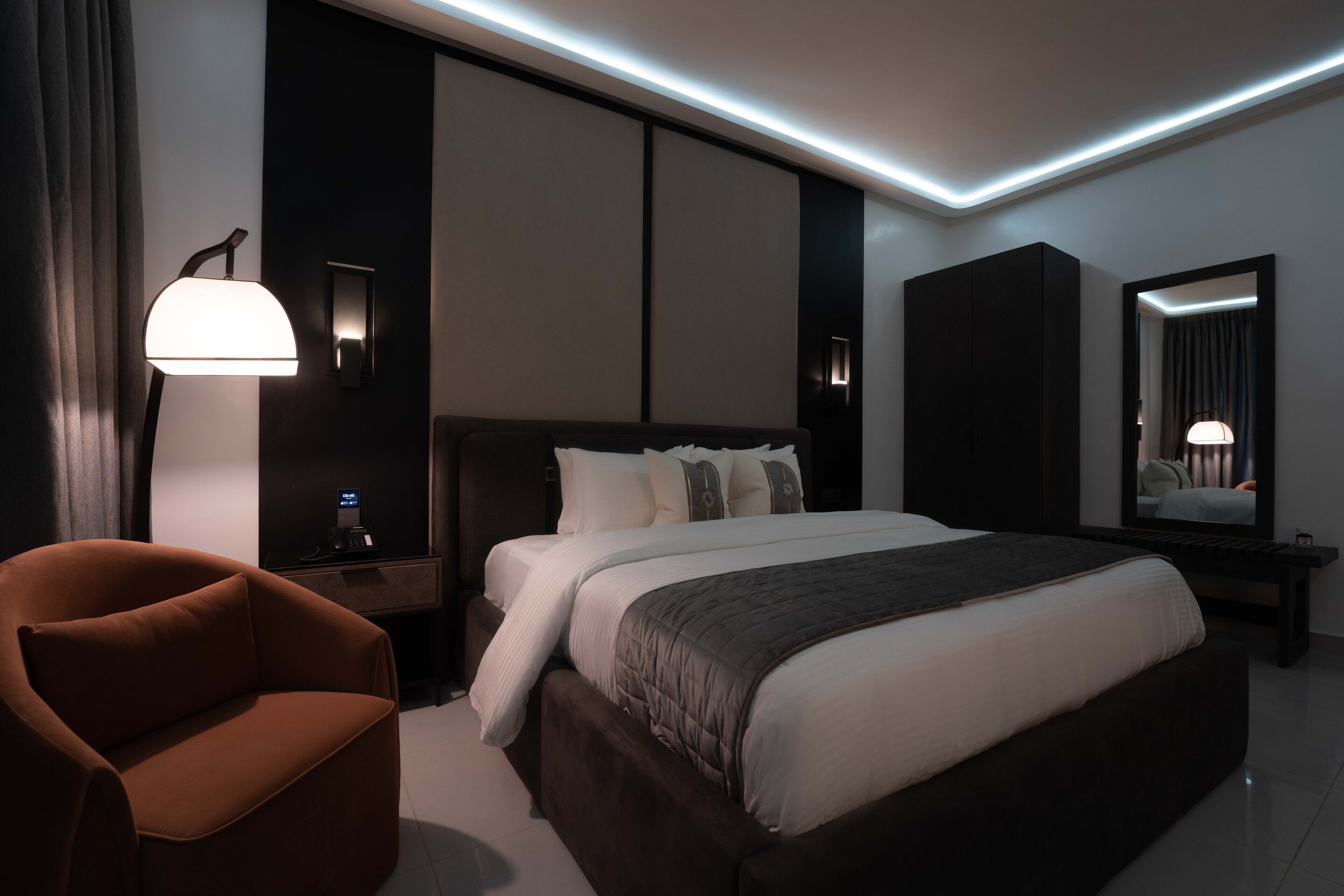 A modern hotel room with a large bed, a nightstand, a desk, a chair, and a mirror.