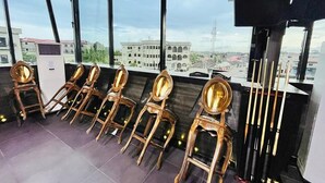 A room with a view of buildings and a pool. There are four wooden chairs with gold accents and a pool table with cue sticks. - Dluxe Premium Hotel (Port Harcourt)