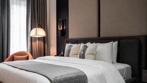 A neatly made bed with a grey quilt, a bedside lamp, and a chair. - Dluxe Premium Hotel (Port Harcourt)