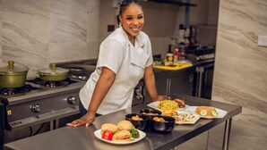 A chef in a white uniform leaning over a counter with various dishes, including burgers and salads, in a modern kitchen with marble walls and stainless steel appliances. - Dluxe Premium Hotel (Port Harcourt)