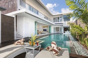 A modern hotel with a large indoor pool, a dining area, and a lounge with seating. - Modern 3 BR Family Villa in the Heart of Legian (Kuta Utara)