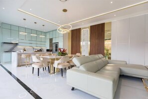 A modern living room with a white sofa, a dining area with a round table, and a kitchen with glass cabinets. - Modern 4 BR Family Villa in the Heart of Legian (Kuta Utara)