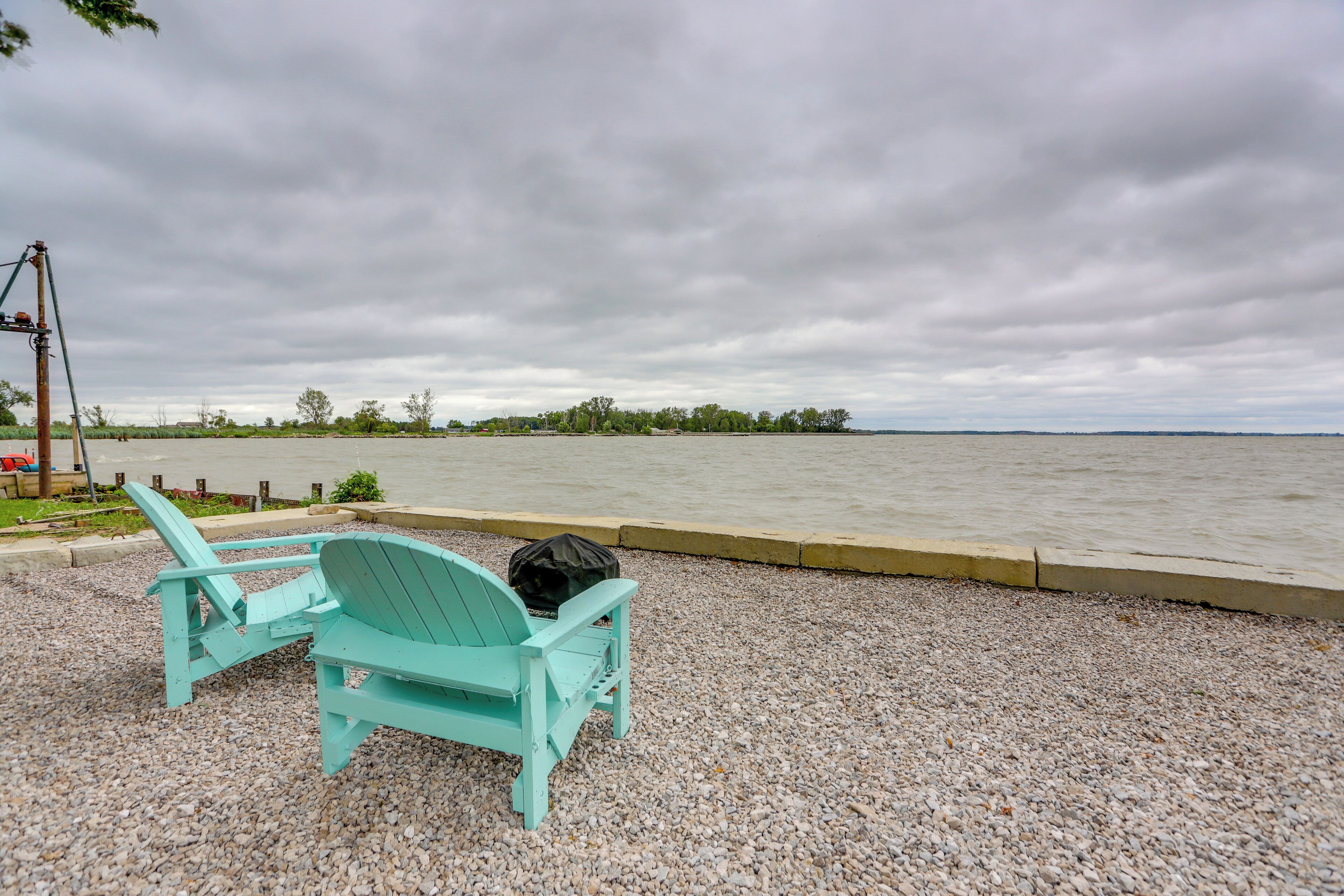 Deux chaises Adirondack turquoise sont placées sur un chemin de gravier, au bord d’une étendue d’eau.