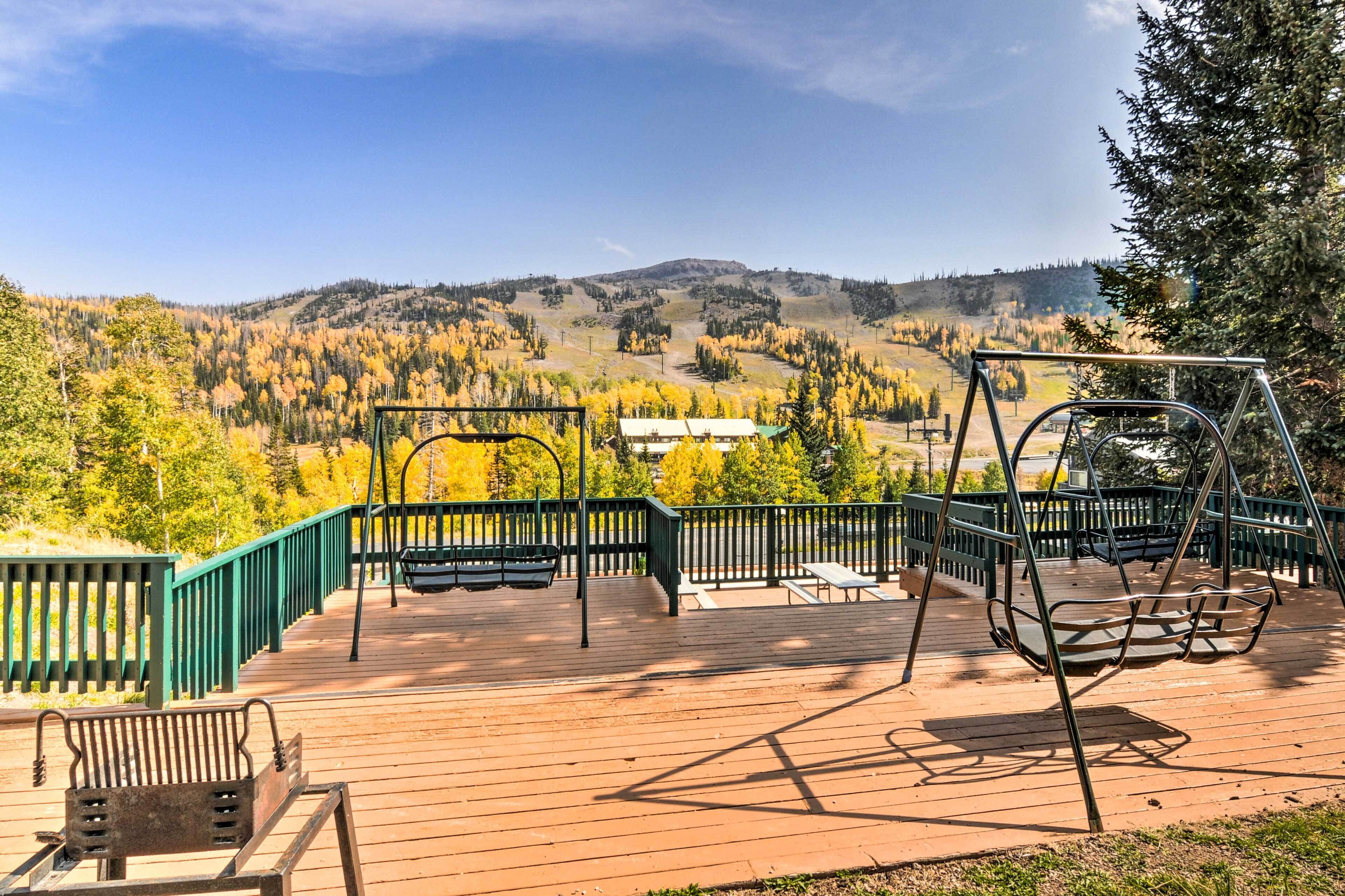 A wooden deck with a swing set and a bench overlooking a forested valley.