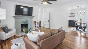Una sala de estar moderna con chimenea, televisor de pantalla plana, ventilador de techo y comedor con candelabro.