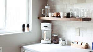 A kitchen with white cabinets, a coffee maker, and shelves holding glasses and cups. - Beautiful & Bright Townhome (Westerville)