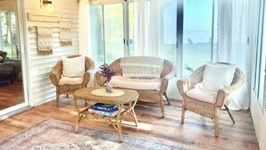 Una habitación acogedora con muebles de mimbre, una mesa redonda de centro y vistas al mar a través de amplias ventanas.