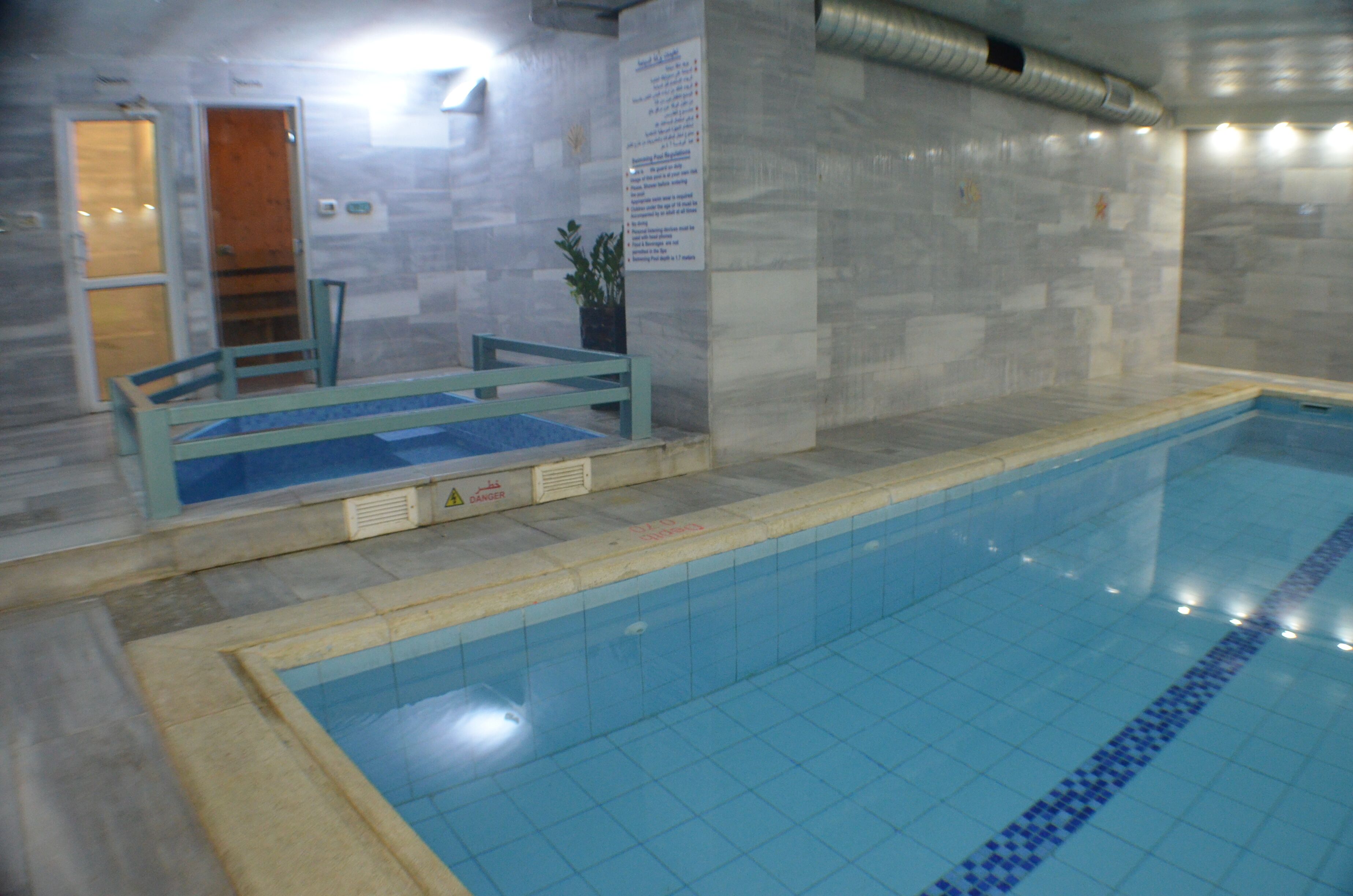 Une piscine intérieure avec des murs carrelés et une zone de pont en bois.