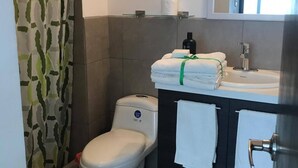 A bathroom with a toilet, a sink with a mirror, and a shower curtain. - Studio apartment great location trendy area (Ciudad de Guatemala)