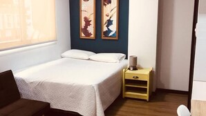 A hotel room with a bed, a small wooden table, a nightstand, a chair, and two abstract paintings on the wall. - Studio apartment great location trendy area (Ciudad de Guatemala)