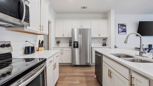 A modern kitchen with white cabinets, stainless steel appliances, and a wooden floor.