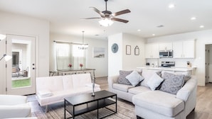 A modern living room with a white sofa, a coffee table, and a dining area with a chandelier.