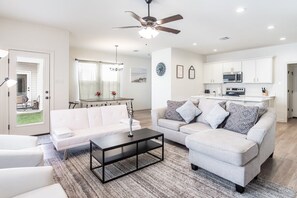 A modern living room with a white sofa, a coffee table, and a dining area with a chandelier. - Tiger Stadium Oasis in Baton Rouge by LSU - CB1014 (Baton Rouge)