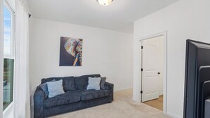 A room with a dark grey sofa, a painting on the wall, a white door, and a ceiling light fixture.