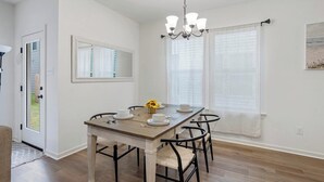 A dining area with a wooden table, black chairs, a chandelier, and a window with curtains. - Tiger Stadium Oasis in Baton Rouge by LSU - CB1014 (Baton Rouge)