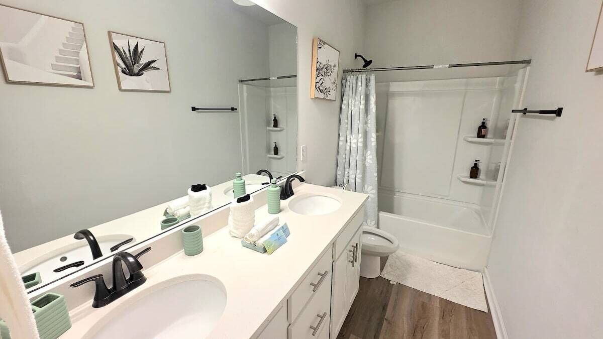 A bathroom with a double sink, a mirror, a shower, and a toilet.