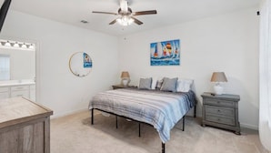 A bedroom with a bed, bedside tables, a ceiling fan, a painting, and a mirror.