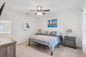 A bedroom with a bed, bedside tables, a ceiling fan, a painting, and a mirror. - Tiger Stadium Oasis in Baton Rouge by LSU - CB1014 (Baton Rouge)
