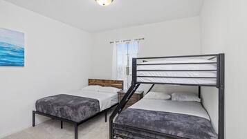 Un dormitorio con literas, un cabecero de madera, una ventana con cortinas y un cuadro en la pared.