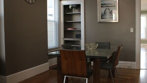 Un coin repas avec une table en verre, deux chaises, une bibliothèque et une horloge au mur.