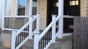 Une maison à deux étages avec un porche à l’avant, une porte noire et une balustrade blanche.