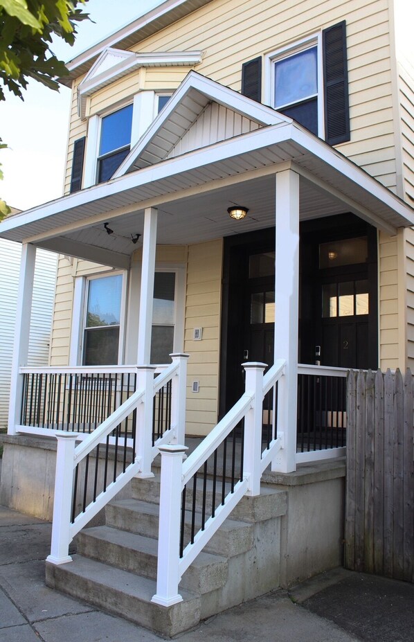 A two-story house with a front porch, a black door, and a white railing. - Watervliet Retreat (Watervliet)