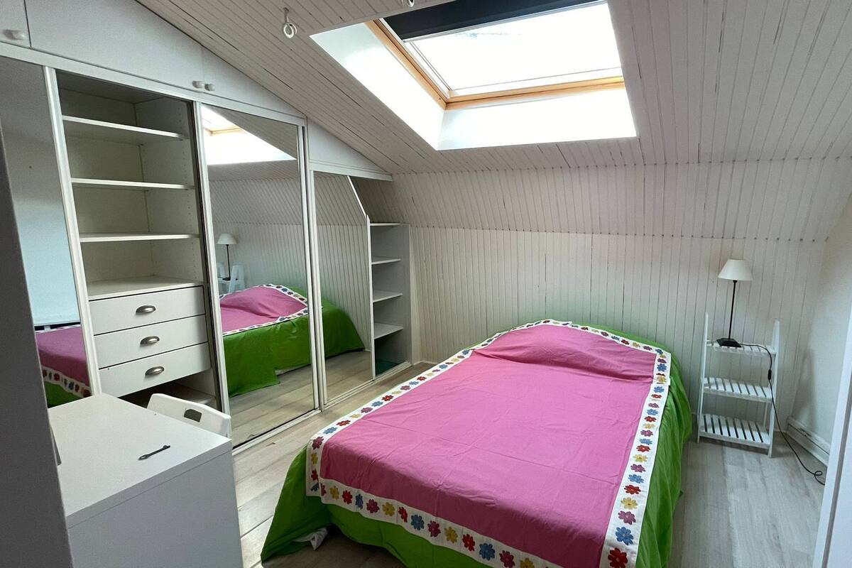 A bedroom with a skylight, a bed with a floral bedspread, a wardrobe, and a bedside table.