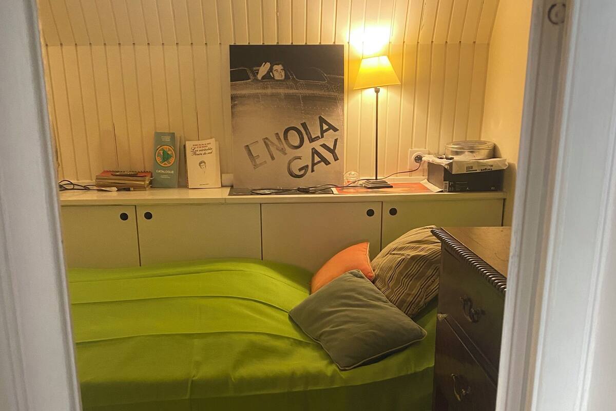 A small, cozy bedroom with a green bed, a poster on the wall, and a lamp.