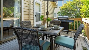 Een terras buiten met een tafel voor vier personen, omringd door rieten stoelen, een barbecue en een grote parasol.