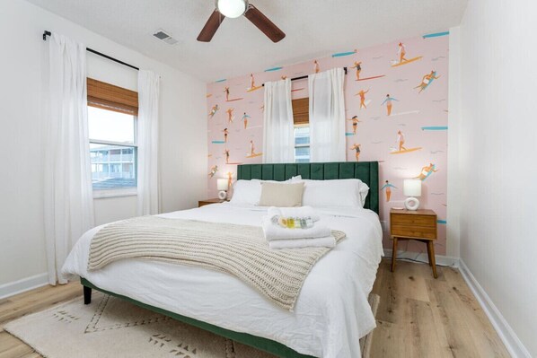 Un dormitorio con cama, ventilador de techo, mesita de noche y una pared decorada con un diseño de personas practicando surf.