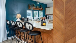 Een moderne keuken met een wit aanrecht, barstoelen, een magnetron en een fles wijn.