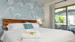 Een net opgemaakt bed met een geruit kussen, een bedlampje en een handdoek met toiletartikelen.