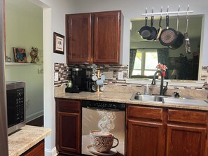 Una cocina con armarios de madera, cafetera, lavavajillas y un colgador para ollas.
