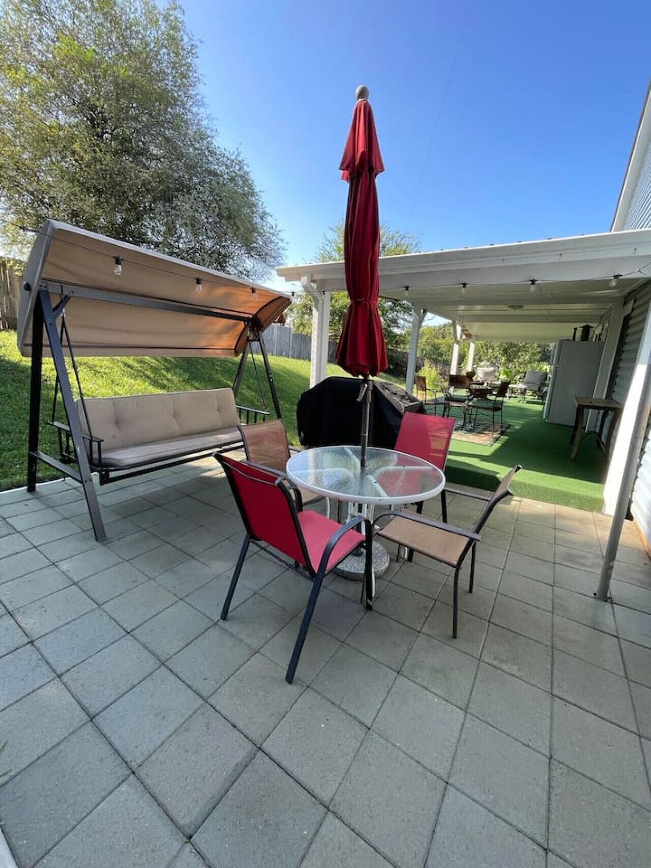 An outdoor patio with a swing set, a round table, and chairs.