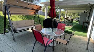 Une terrasse extérieure avec une balançoire, une table ronde et des chaises.