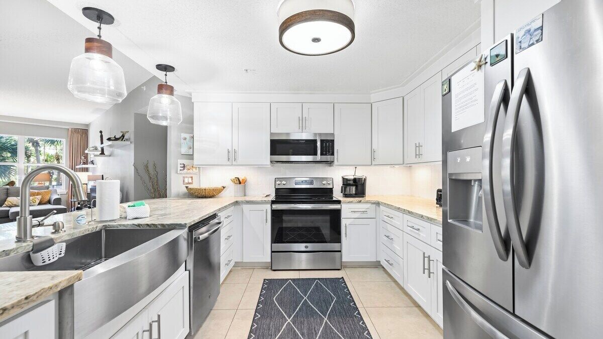 A modern kitchen with stainless steel appliances, white cabinets, and pendant lighting.