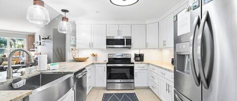 A modern kitchen with stainless steel appliances, white cabinets, and pendant lighting.