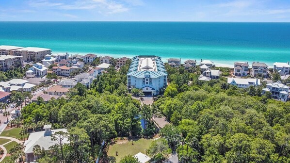 Un área residencial costera con un edificio destacado de techo azul y paredes blancas, rodeado de vegetación exuberante y una vista despejada del océano.