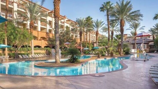 Ein Hotelpoolbereich mit mehreren Pools, Palmen und Liegestühlen.