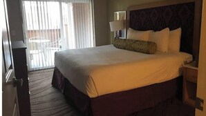 Ein Hotelzimmer mit einem großen Bett, einem Nachttisch, einer Lampe und Blick auf den Balkon.