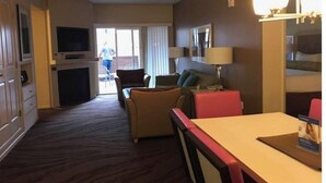 Ein Hotelzimmer mit Essbereich, einer Couch, einem Fernseher und einer Schiebetür zu einem Außenbereich.