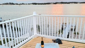 Een terras met een rieten bank, een champagnefles en twee glazen op een dienblad.