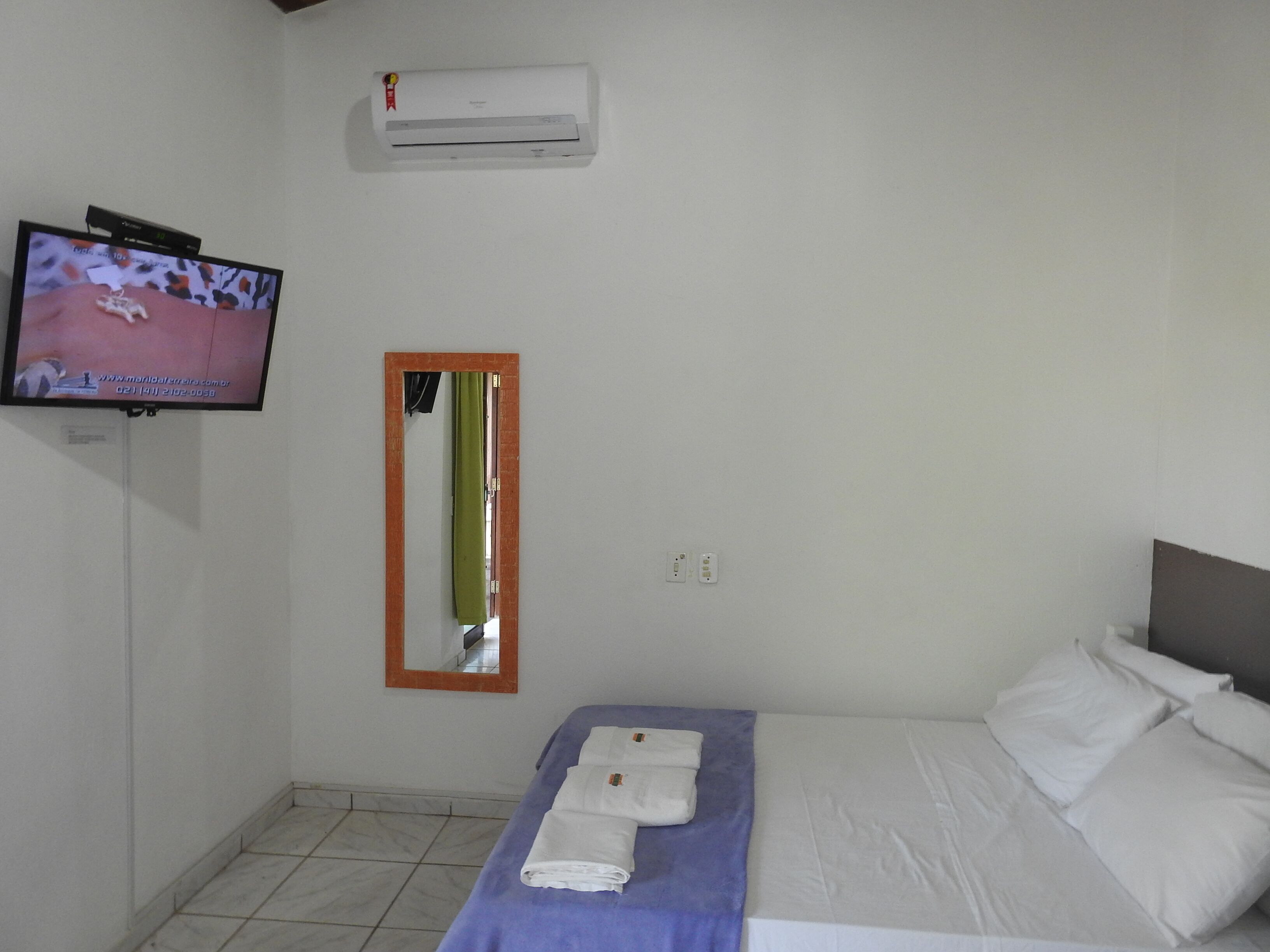 A hotel room with a bed, a TV, an air conditioner, and a mirror.