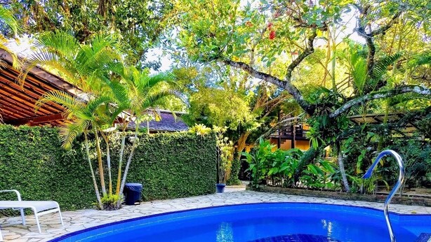 A swimming pool with a tiled edge, surrounded by a stone patio and lush greenery. - Recanto Primavera - Camburi (São Sebastião)