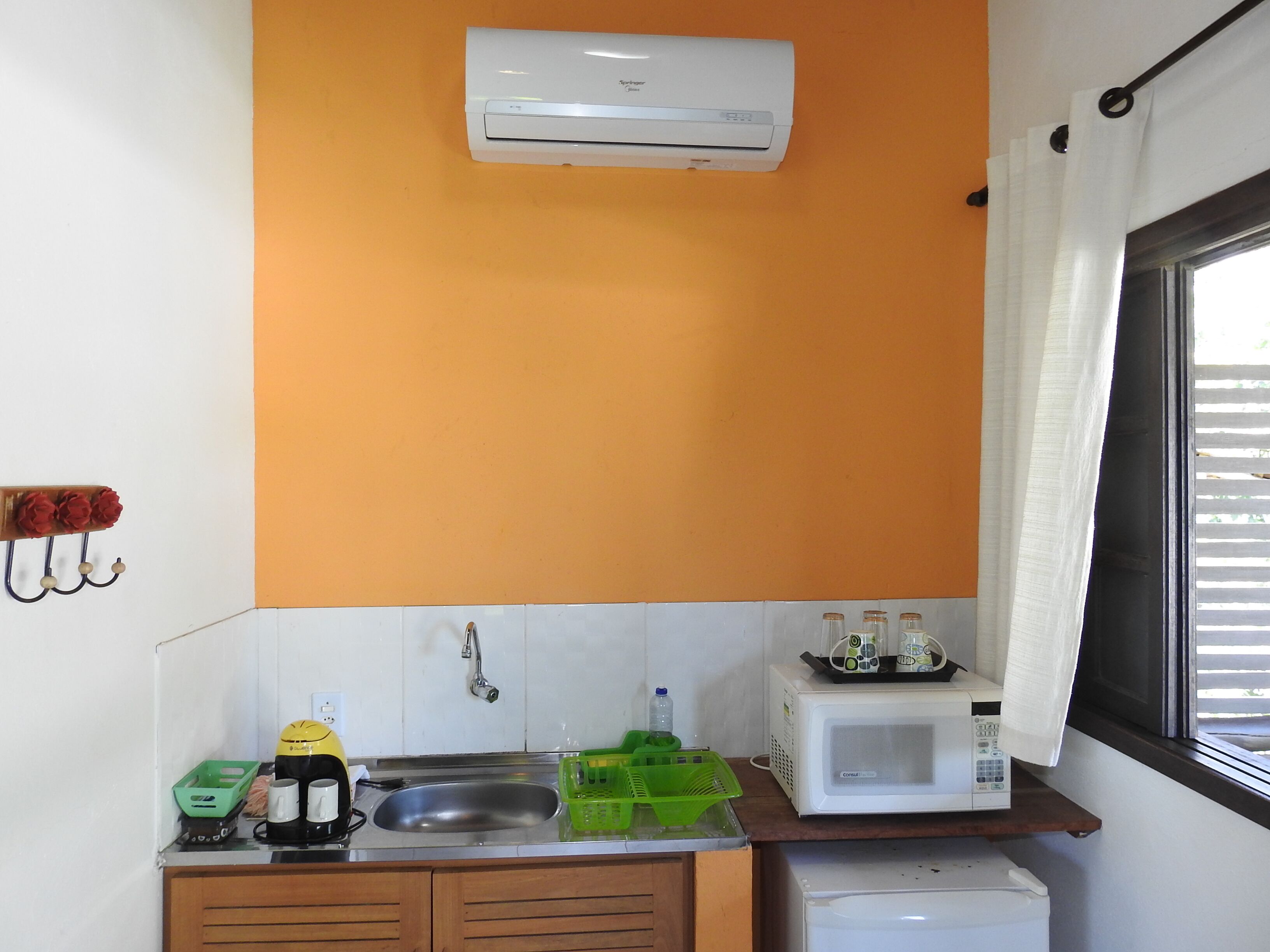 Uma cozinha compacta com pia, micro-ondas e geladeira pequena.