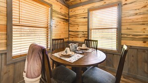 Une pièce aux murs lambrissés, avec une table ronde dressée pour quatre personnes, agrémentée d’une carafe, d’un saladier et d’une assiette.