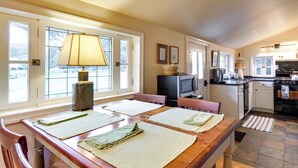 A kitchen with a wooden table, chairs, a television, and a stove. - Monticello Wine Trail Cottage - Close to Hiking! (Afton)